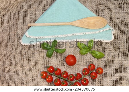 Funny face made of cherry tomatoes ,basil leaves and a napkin and wooden spoon as a hat, over jute tablecloth. Original set table