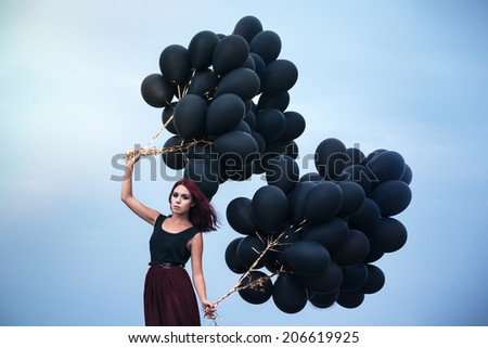 Beautiful girl walking in the beach while holding black balloons