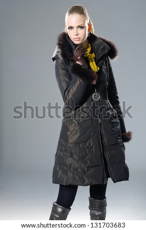fashion model in coat holding little purse posing on light background