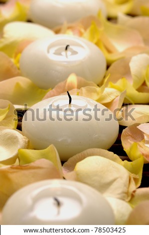 Three white candle and rose petals on mat