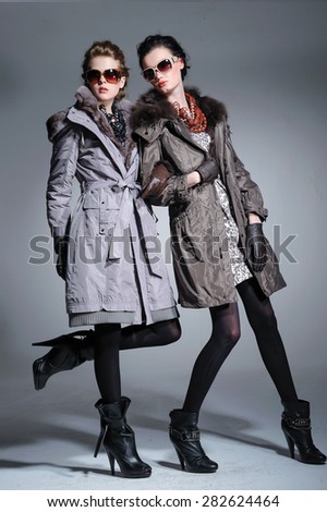 full-length fashion two model in coat clothes with sunglasses posing on light background