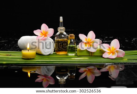 Still life with pink frangipani and candle, oil, towel with row of plant stem