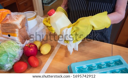 Coronavirus pandemic. Wiping food packages after shopping for groceries. Woman wearing gloves and using disinfectant sanitizing wipes to clean grocery items to prevent the spread of the COVID-19 virus
