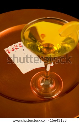 Yellow cocktail and royal flush on a bronze tray with black background.  Focus on the royal flush