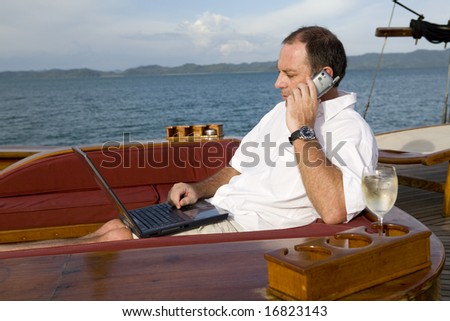 Handsome man on deck of yacht with mobile phone and laptop