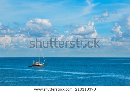 Isolated sailboat on blue ocean sea with white fluffy clouds in clear blue sky looking restful relaxing calm isolated secluded private
