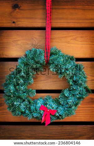 Green fir nondenominational Christmas holiday wreath with small red bow hanging on wooden planks with retro vintage filter