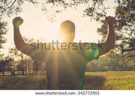 Successful happy accomplished man stands with raised arms facing the sun. White male athlete with arms up celebrating and happy with his achievement and exercise with a retro vintage filter.
