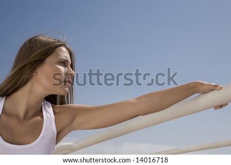 Beautiful young woman standing against a fence on a ship and looks ahead.