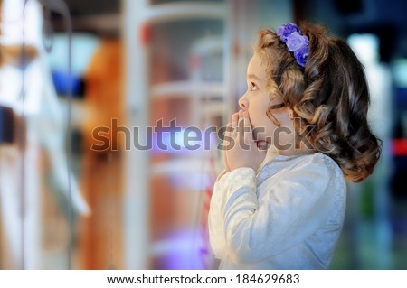 Little cute girl looking at shop window in the mall. Admiration, surprise, delight, joy.