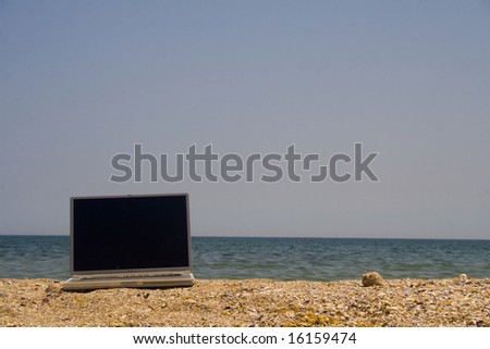 Laptop sitting on sand with sea and blue sky behind