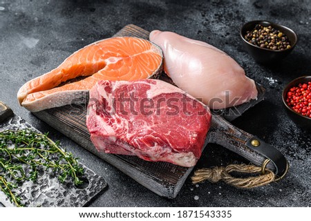 Set of raw meat steaks salmon, beef and chicken on a cutting board. Black background. Top view