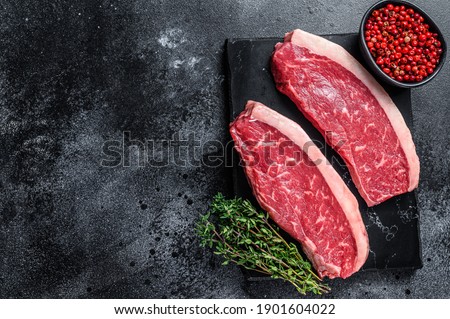 Raw cap rump steak or top sirloin beef meat steak on marble board. Black background. Top view. Copy space.