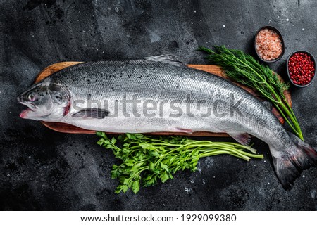 Uncooked raw sea salmon whole fish on a wooden board with herbs. Black background. Top view. Foto d'archivio © 