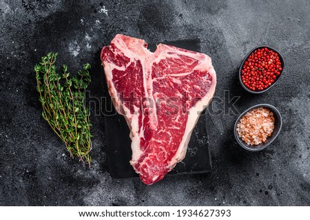 Dry-aged Raw T-bone or porterhouse beef meat Steak with herbs and salt. Black background. Top view.
