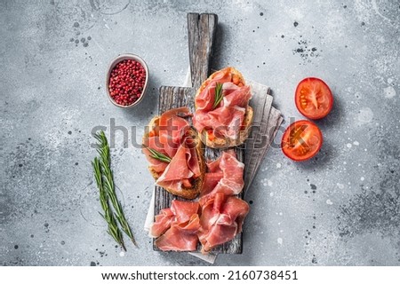 Spanish Tapas - Toast with tomatoes and cured Slices of jamon iberico ham on wooden board. Gray background. Top view. Foto stock © 