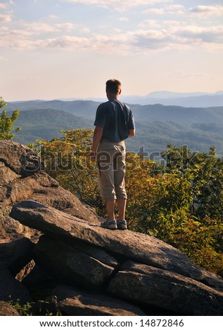 Hiker standing on rock outcroppings while looking out over mountains in the late afternoon.
