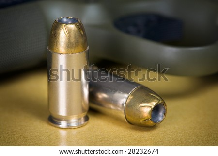 .45 Caliber Hollow Point Pistol Bullets Standing Near Handgun on gold colored background