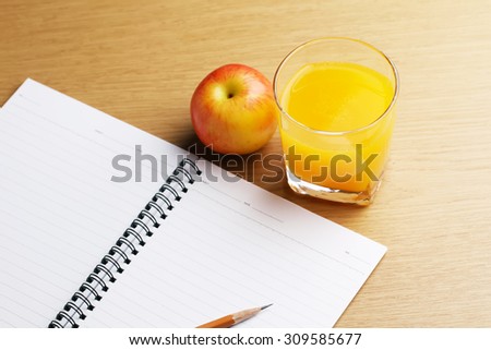 Glass of orange juice with a note book on wood background.