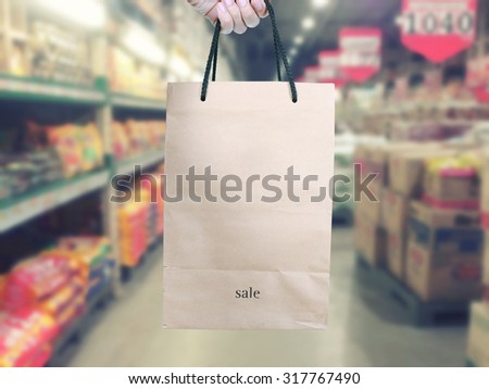 Abstract blur shopping mall with hand holding brown paper shopping bag.store blur background.