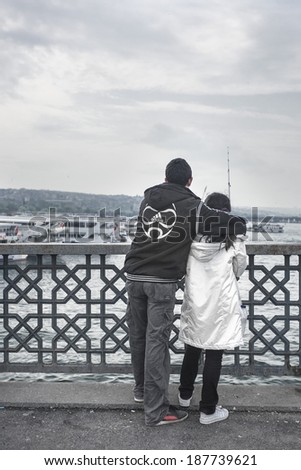ISTANBUL, TURKEY - MAY 20, 2011: A young man embraces a young woman, and tries to teach her how to fish with a fishing pole, in Galata bridge, in Istanbul. A famous fishing place for locals.