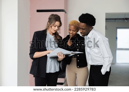 Blonde young realtor is seen giving a tour of a spacious apartment to an African couple. The couple appears to be comparing different units as they discuss which one would best meet their needs. Stock foto © 