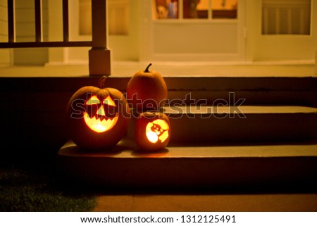 Two jack o' lanterns glowing on the steps of a house beside a normal pumpkin. Foto stock © 