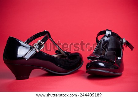 Black shine leather girl shoes with black ribbon isolated on red