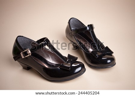 Black shine leather girl shoes with black ribbon isolated on cream