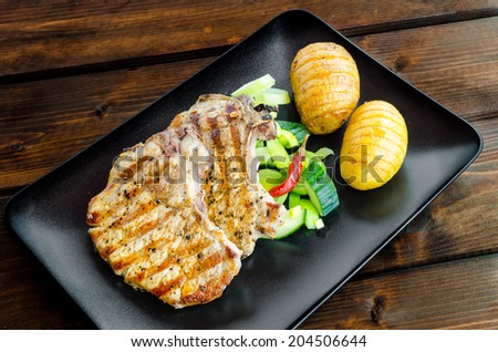 Grilled cutlet with vegetables and roasted potatoes on dark plane