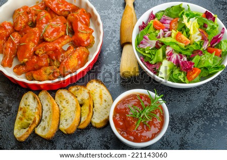 Hot chicken wings with spicy habanero sauce and mixed salad with cherry tomatoes, grilled baguette with olive oil
