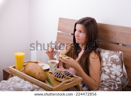 Beautiful young woman eating breakfast in bed in the morning, complete breakfast spread butter