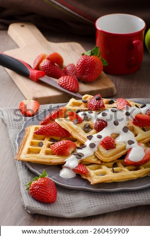 Homemade waffles with maple syrup and strawberries, topped cream and chocolate chips, orange fresh beverage