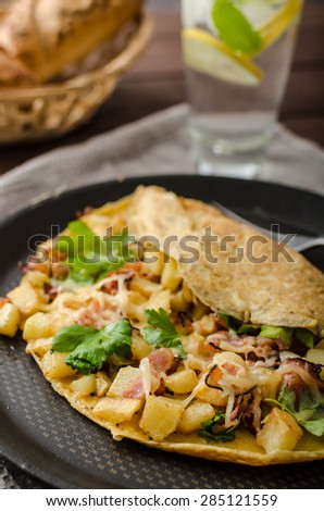 Country egg omelette filled bacon, parsley and potatoes, sprinkled with cheese and herbs
