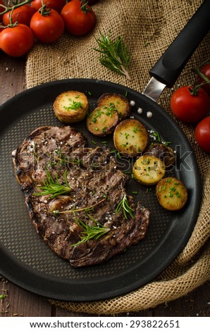 Beef rib eye steak with rustic potatoes, fresh herbs and tomatoes, sprinkled sea salt and herbs