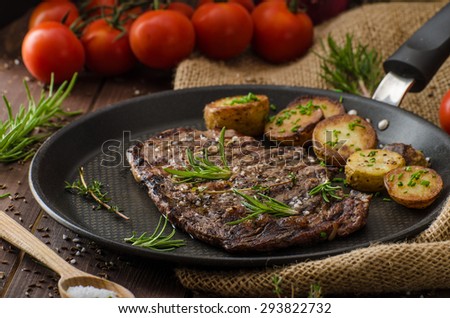 Beef rib eye steak with rustic potatoes, fresh herbs and tomatoes, sprinkled sea salt and herbs