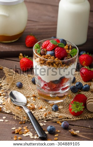 Yogurt with baked granola and berries in small glass, strawberries, blueberries. Granola baked with nuts and honey for little sweetness. Homemade yogurt