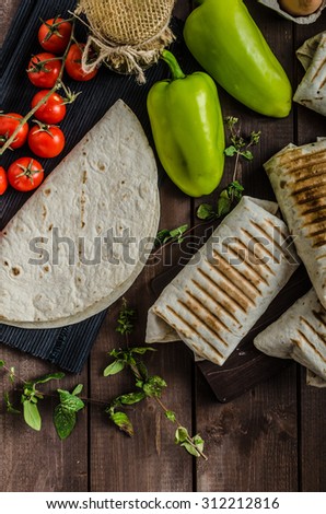 Breakfast burrito on wood board and wood table, eggs, pepper, potatoes and meat inside