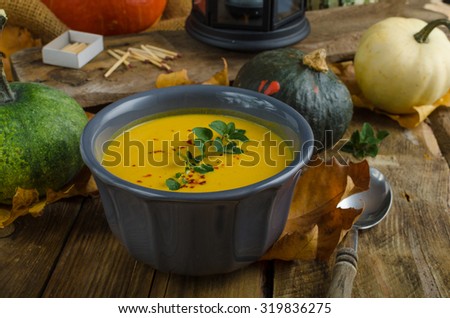 pumpkin soup with chilli and herbs, nice autumn leaves and rustic wood table