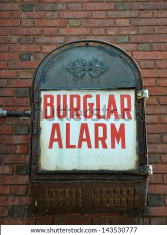 A vintage burglar alarm mounted on a brick wall