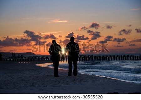 Silhouette of couple taking a walk on a beach shore in sunset light