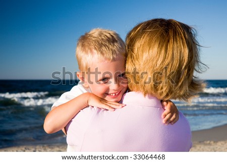 3 years old boy hugging his mother on a beach in sunny day