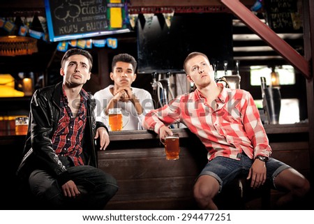 Watching TV in bar. happy young men drinking beer and gesturing while sitting in bar