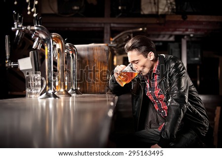 It was a hard day. Depressed young man drinking beer in bar and holding hand in hair