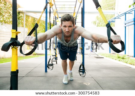 Man during workout with suspension straps on the street. Trx
