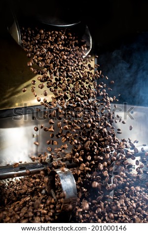 The freshly roasted coffee beans from a coffee roaster being poured into the cooling cylinder. Frozen moment.