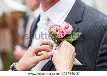 bridesmaid adjusting flower on groom\'s jacket
