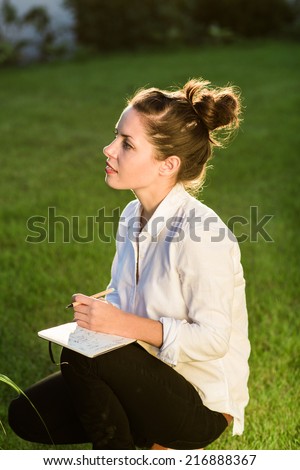 Young happy businesswoman or landscape architect sitting in the garden with her notebook. Young professional is dressed in casual clothes.