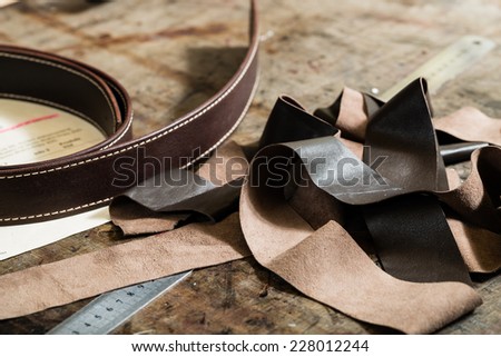Leather belt, iron ruler and remainders of the leather on the working desk in the leather workshop.