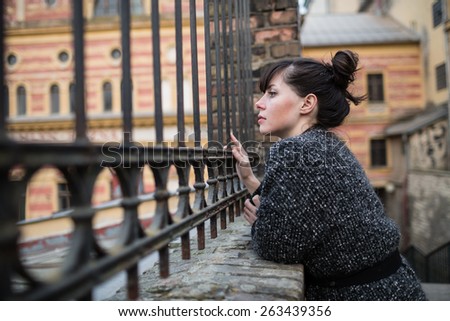 A young woman looking into the old building or factory through the iron fence with vintage ornament.